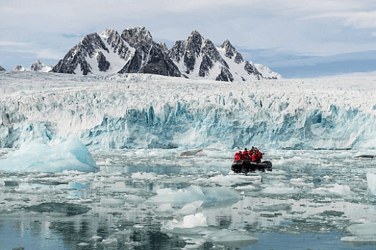 Ein Schlauchboot mit Teilnehmern der Expeditionskreuzfahrt fährt durch Eisschollen entlang einen großen Gletscher in Spitzbergen