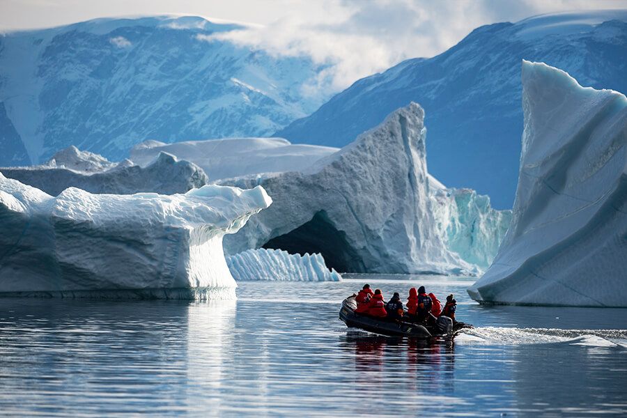 Kreuzfahrt-Gäste in roten Expeditions-Parkas fahren in Schlauchbooten durch schwimmende Eisberge in Grönland