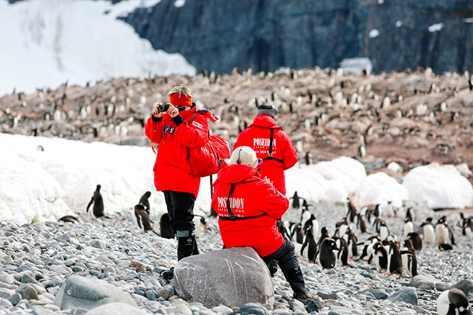 Drei Kreuzfahrtgäste in roten Paraks fotografieren Pinguine in der Antarktis