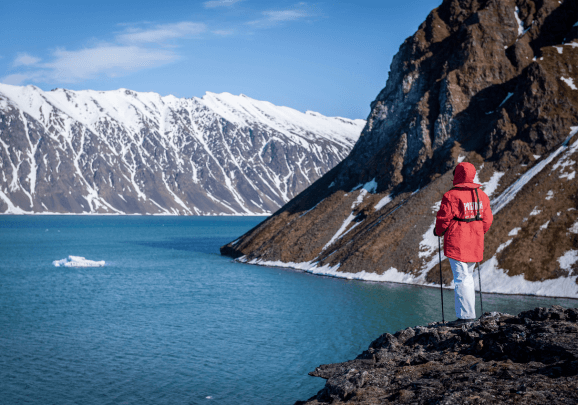Ein Gast der Expeditionskreuzfahrt schaut auf einen Fjord und schneebedeckte Berge in Spitzbergen