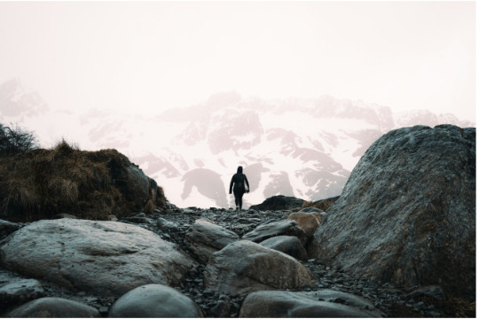 Wanderer in felsiger Landschaft in Ushuaia. Im Hintergrund hohe schneebedeckte Berge.