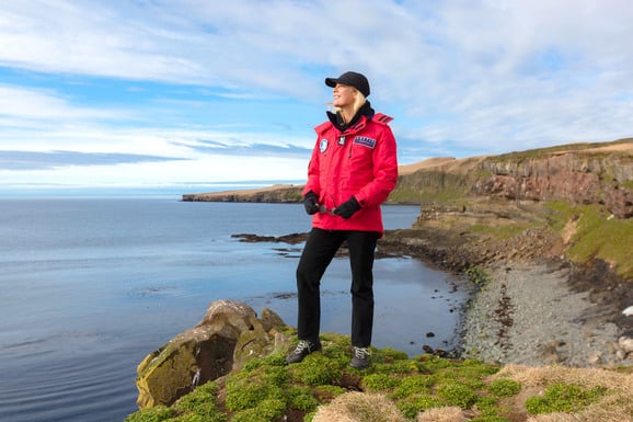 Kreuzfahrt Gast steht im roten Expeditionsparka auf einer Steilklippe in Island
