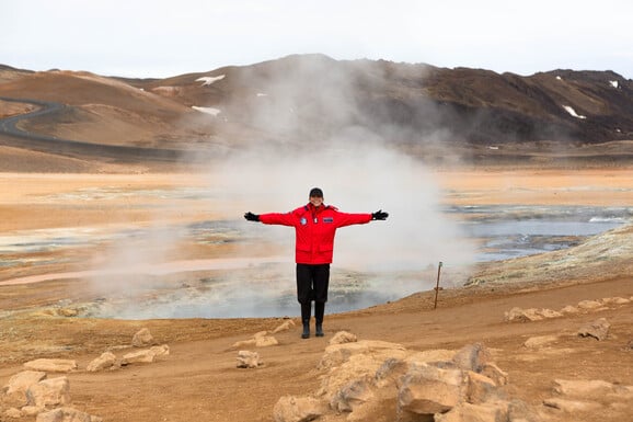 geothermische Quellen in Hverir auf Island vor denen ein Gast der Kreuzfahrt steht und die die Arm ausbreitet