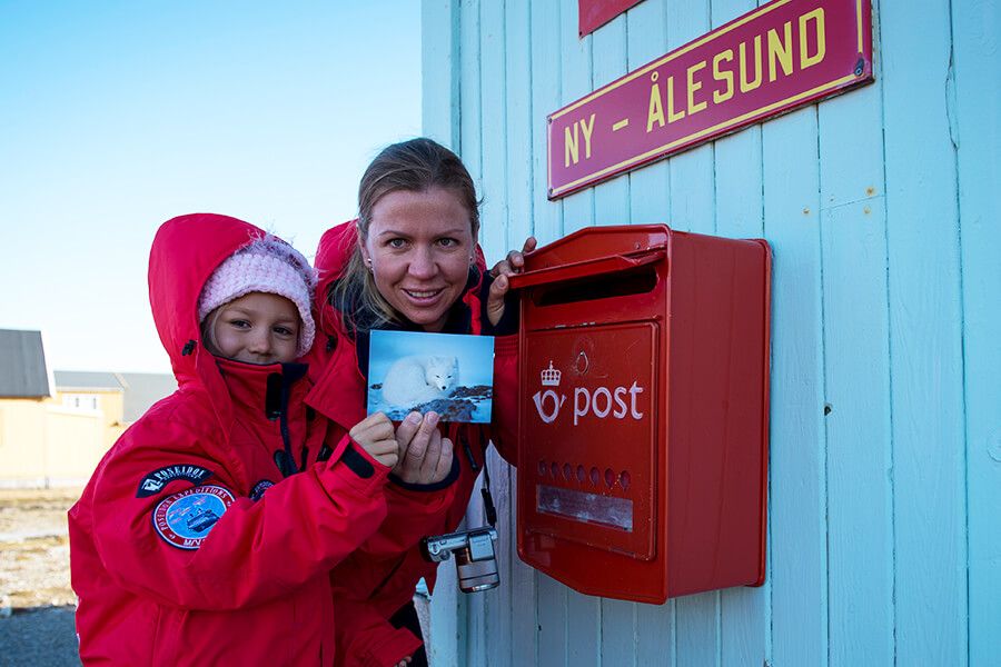 Ein Postkarte mit einem Polarfuchs wird in Ny-Ålesund auf Spitzbergen von zwei Kreuzfahrtgästen in den nördlichsten Briefkasten der Welt geworfen