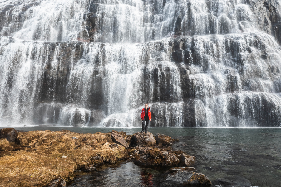 Ein großer Wasserfall auf Island vor dem ein Gast der Expeditionskreuzfahrt steht