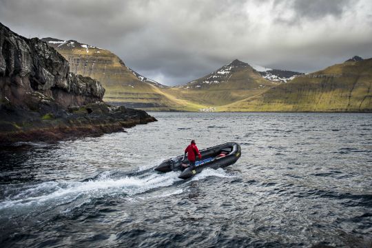 Schlauchboot fährt in einen Fjord mit schneebedeckten Bergen bei der Kreuzfahrt durch die britischen Inseln