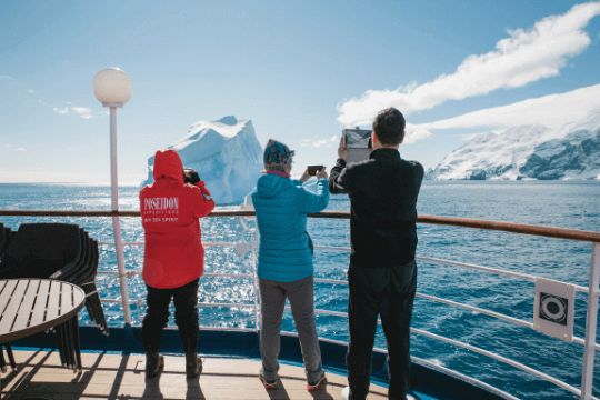 Gäste mit Handys und Kameras an Deck des Expeditionskreuzfahrtschiffs fotografieren einen Eisberg