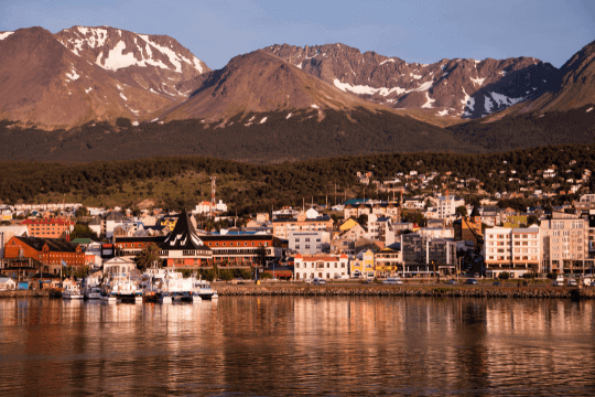 Hafen von Ushuaia mit Blick auf die Stadt und schneebedeckten Bergen im Hintergrund. Im Hafen liegen Kreuzfahrtschiffe die Richtung Antarktis starten.