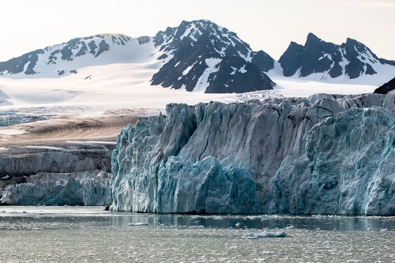 Ein großer Gletscher in einem Fjord auf Spitzbergen vor dem viele kleine Eisschollen schwimmen