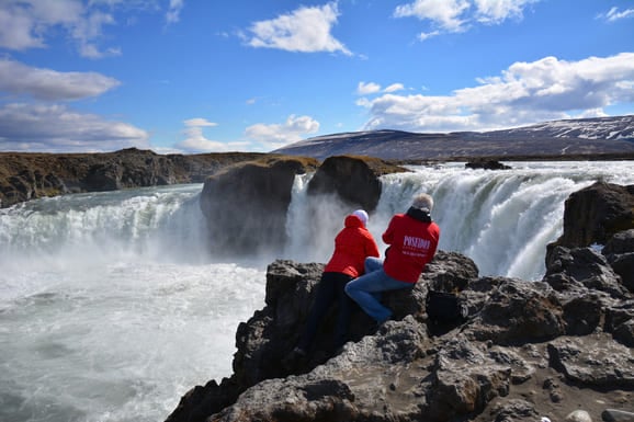 Zwei Gäste von der Kreuzfahrt machen auf Island Fotos von einem Wasserfall