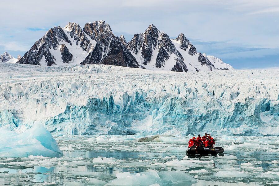 In einem Schlauchboot sitzen Fotografen mit ihren Kameras und fahren entlang eines Gletschers vor Spitzbergen