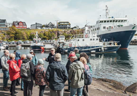Wir besuchen auf der Kreuzfahrt Plantagen in Tórshavn. Unsere Reisegruppe steht mit einem Führer im Hafen und lässt sich Tórshavn erklären