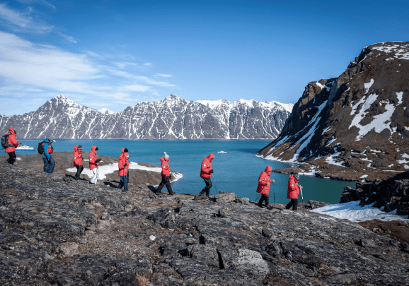 Eine Gruppe Kreuzfahrtgäste wandert entlang der Küstenlinie on Spitzbergen