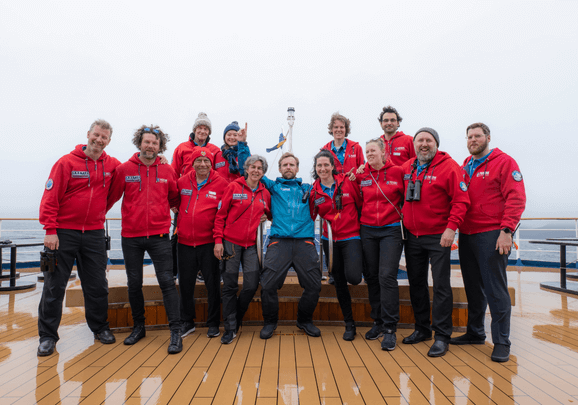 Trotz Regen hat die Expeditionscrew an Bord des Kreuzfahrtschiffs gute Laune beim Abschiedsbild im Hafen von Reykjavík auf Island