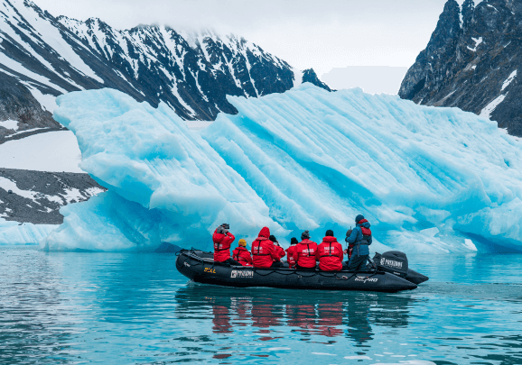 Gäste einer kreuzfahrt in einem Schlauchboot umfahren einen großen Eisberg der in einem Fjord in Spitzbergen treibt
