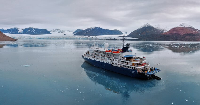Vor einem Gletscher an Spitzbergens Küste liegt das Kreuzfahrtschiff in spiegelglatten Wasser kayaking-in-svalbard-4