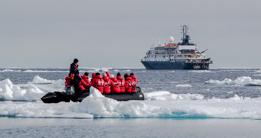 Ein Zodiac Schlauchboot mit Expeditionsmitgliedern im Packeis, im Hintergrund ist das Schiff zu sehen. expedition-ships-cruising