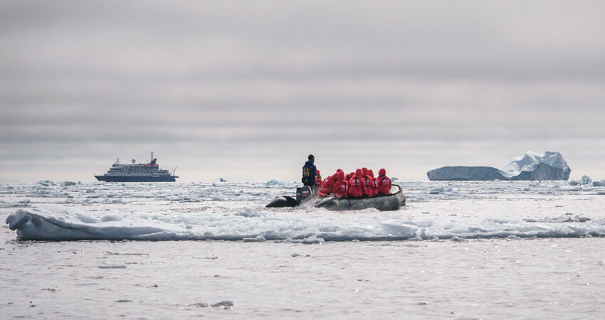 Zodiac vor Grönlands stürmischer Küste, im Hintergrund das Expeditionsschiff 02-Zodiac-und-Eis