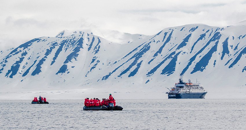 Zodiac, die vor einer eisigen Küste im Meer treiben, im Hintergrund ist das Expeditionsschiff zu sehen. expedition-ships-cruising-alone